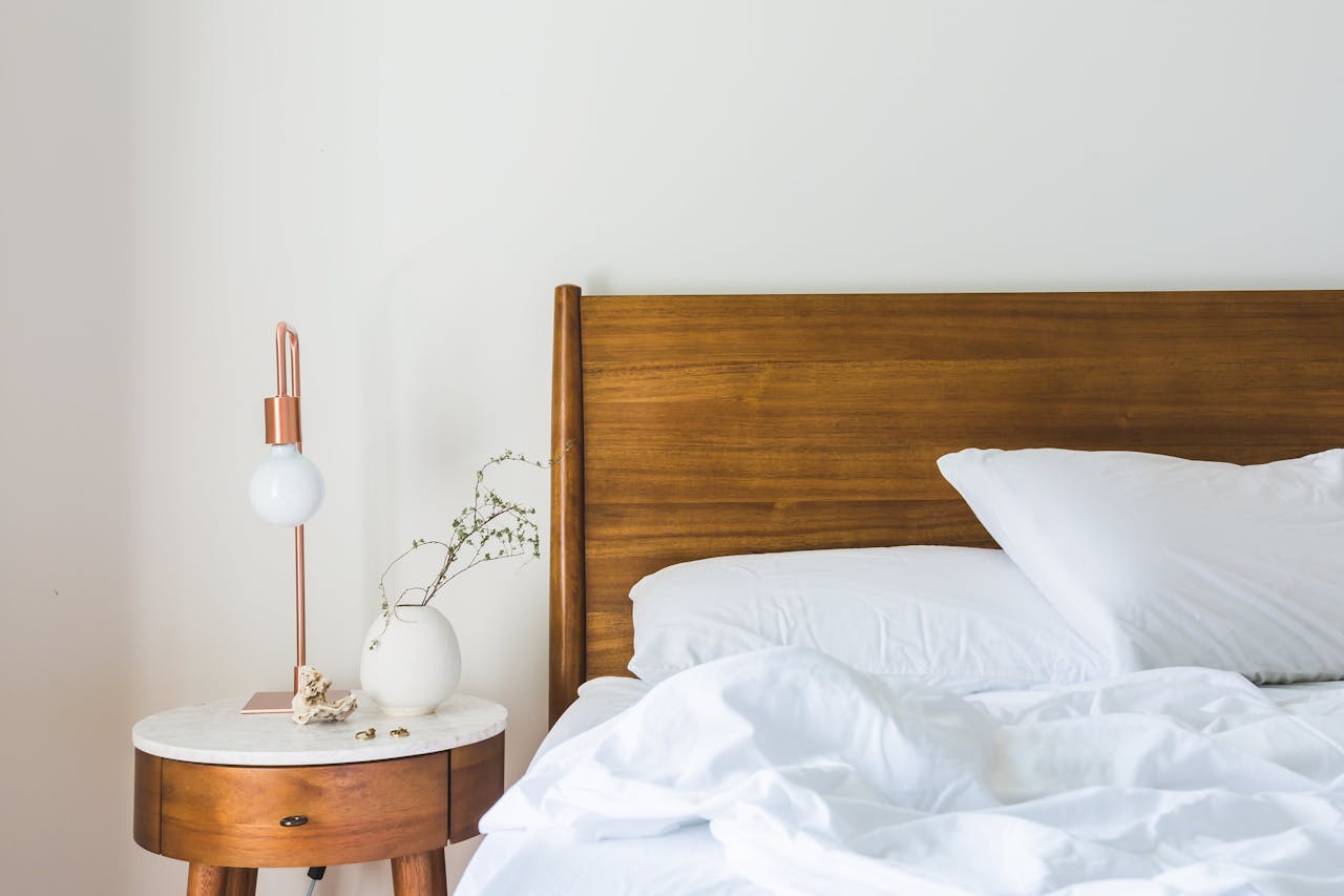 hero-img A minimalist bedroom features a wooden headboard, white bedding, and a stylish side table lamp.